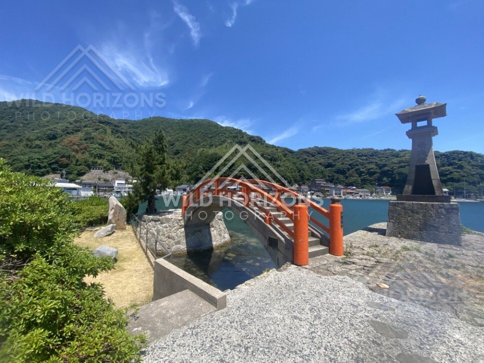 Stone lantern overlooking the red arch of Bentenjima Bridge and the bay. Mihonoseki, Japan.
