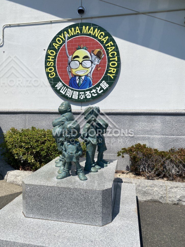 Bronze character statues beneath the Gosho Aoyama Manga Factory wall logo. Hokuei, Japan.