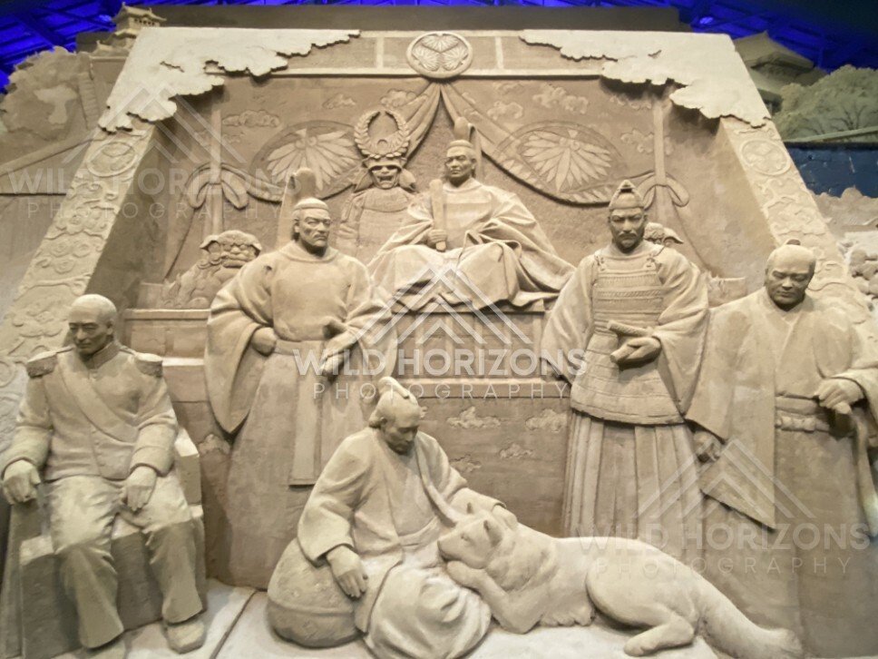 Wide View of Sand Sculpture Panel with Figures and Resting Dog. Tottori Sand Museum, Japan.