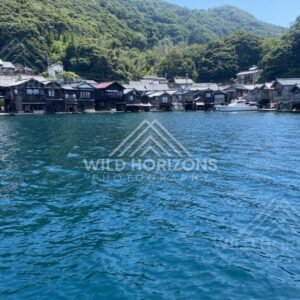 A white motorboat anchored near the funaya boathouses under a clear sky. Ine, Japan