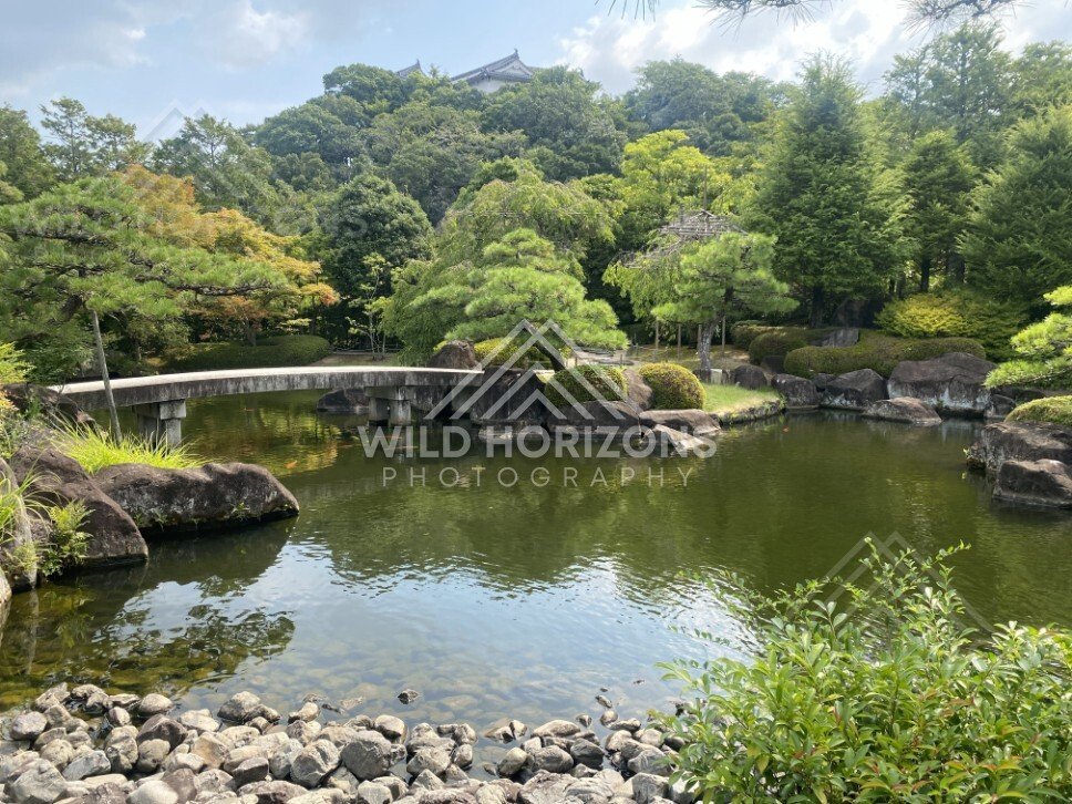 Curved Stone Bridge and Rock Garden Beside a Still Pond. Koko-en Garden, Japan.