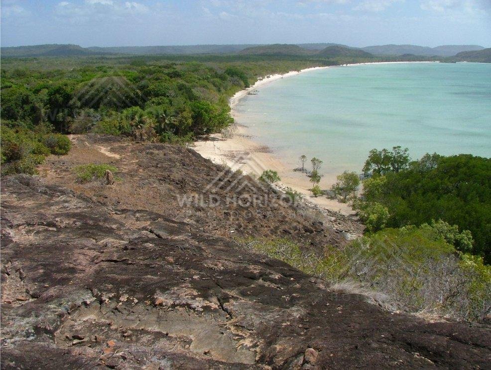 Curving tropical beach backed by coastal woodland from a rocky ridge. Seisia, Australia.