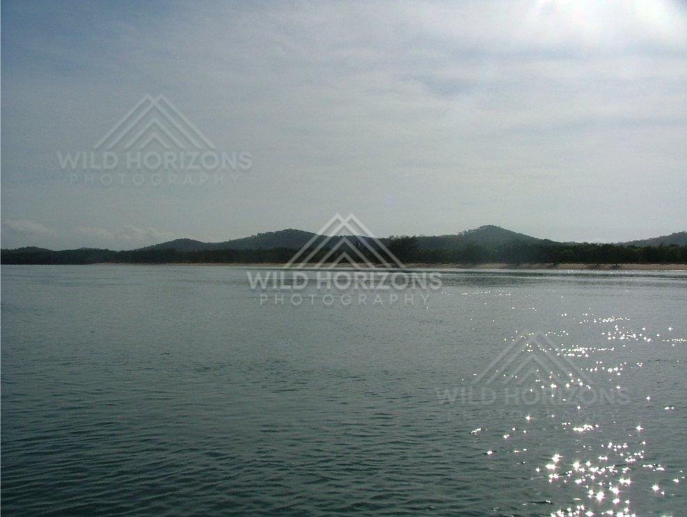 Sunlit bay with distant forested hills across calm water. Seisia, Australia.