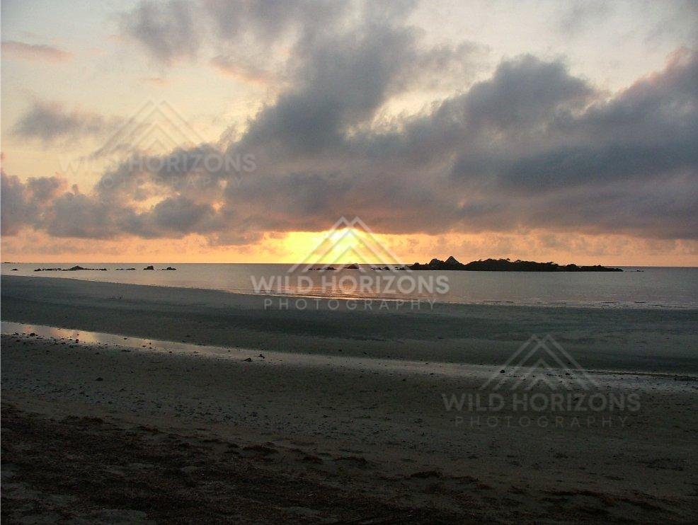 Sunset over calm ocean with dramatic storm clouds and distant rocky islets. Cape York, Australia.