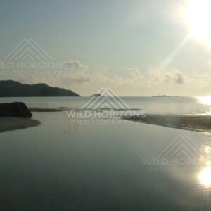 Sun glare over calm sea and reflective tidal pool at low tide. Chili Beach, Australia.