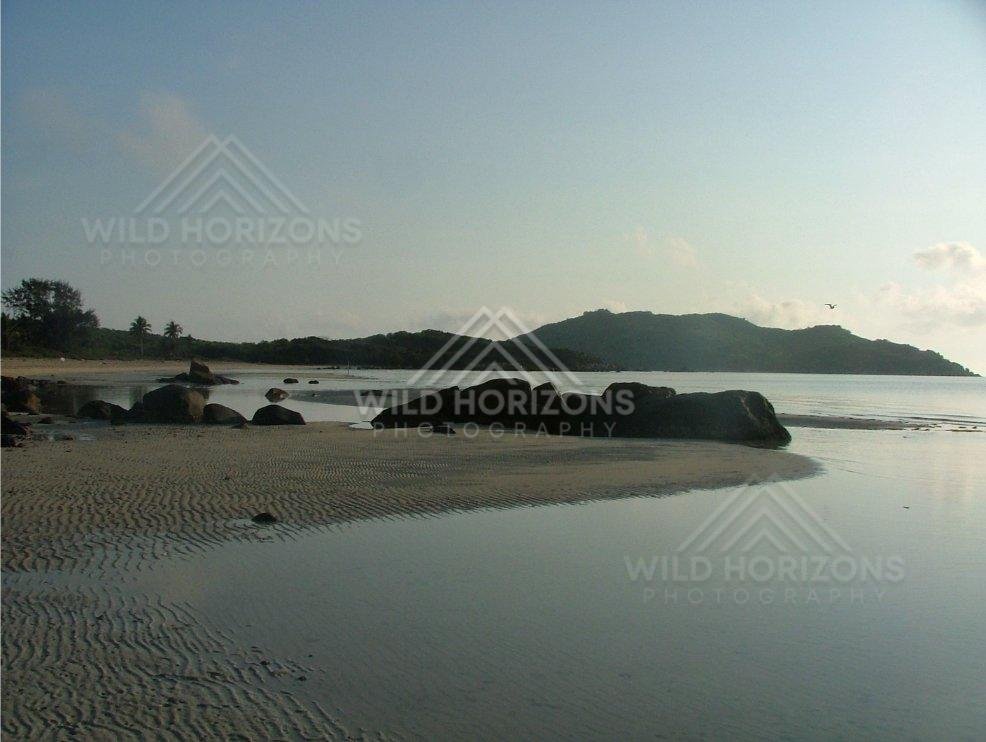 Rippled sand flats with granite boulders beside a quiet bay. Chili Beach, Australia.