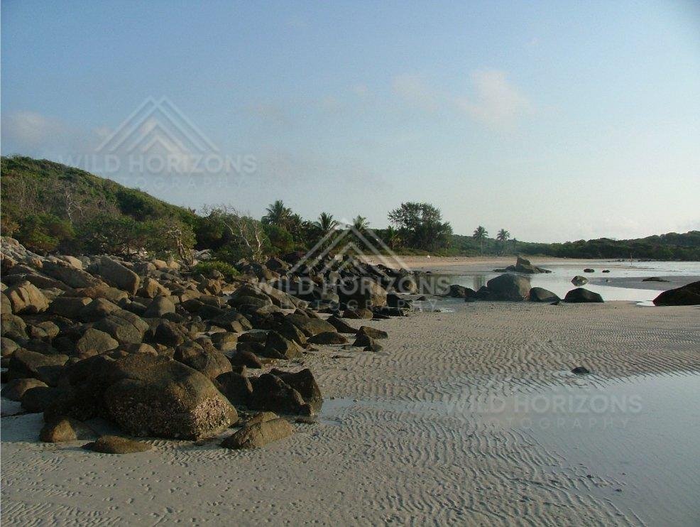 Rocky shoreline and sand ripples along a sheltered tropical beach. Chili Beach, Australia.