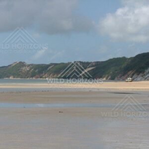 On a bright afternoon at Elim Beach, calm shallow waters reflect distant cliffs and open skies. Elim Beach, Australia.