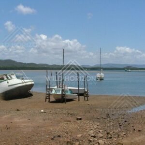 Within Cooktown harbour, small fishing vessels rest on mud flats at low tide beneath blue skies. Cooktown, Australia.