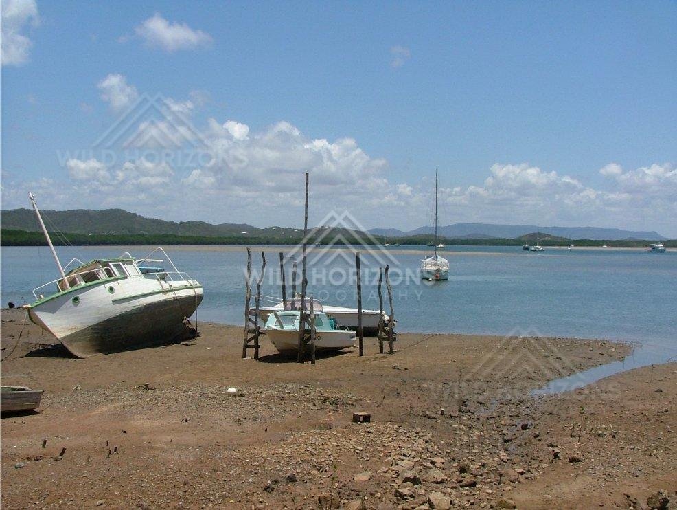 Within Cooktown harbour, small fishing vessels rest on mud flats at low tide beneath blue skies. Cooktown, Australia.