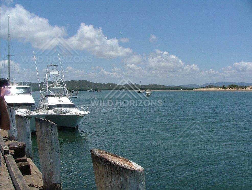 From the wharf at Cooktown, boats lie moored overlooking the wide blue bay. Cooktown, Australia.
