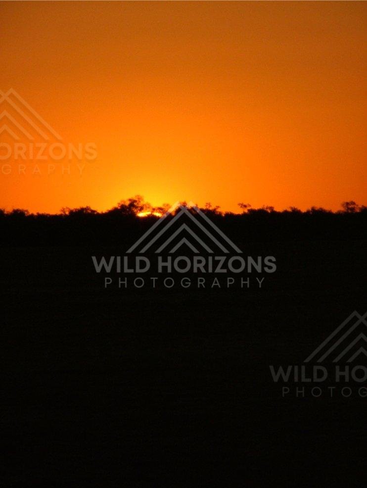 Over the Simpson Desert, a fiery sunset sky silhouettes the remote horizon. Simpson Desert, Australia.