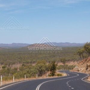 In the Cape York Area, a sealed highway winds through open savanna woodland toward distant ranges. Cape York Area, Australia.
