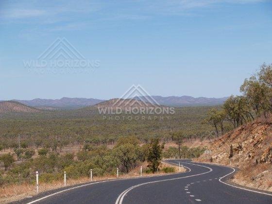 In the Cape York Area, a sealed highway winds through open savanna woodland toward distant ranges. Cape York Area, Australia.