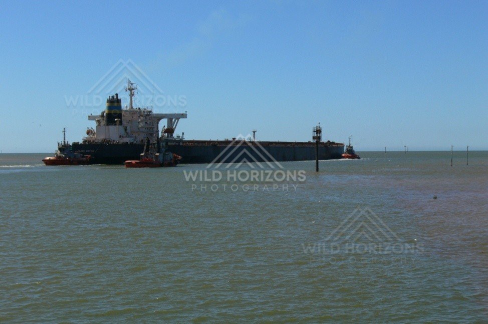 Tugboats guiding a loaded ore ship from Port Hedland channel. Pilbara, Australia.