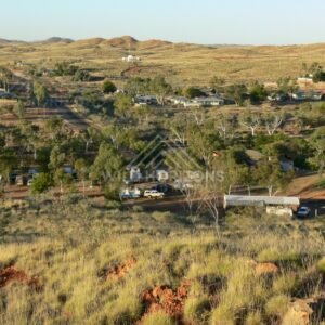 Outback township and caravan park among eucalypt trees with low ironstone hills beyond. Pilbara, Australia.