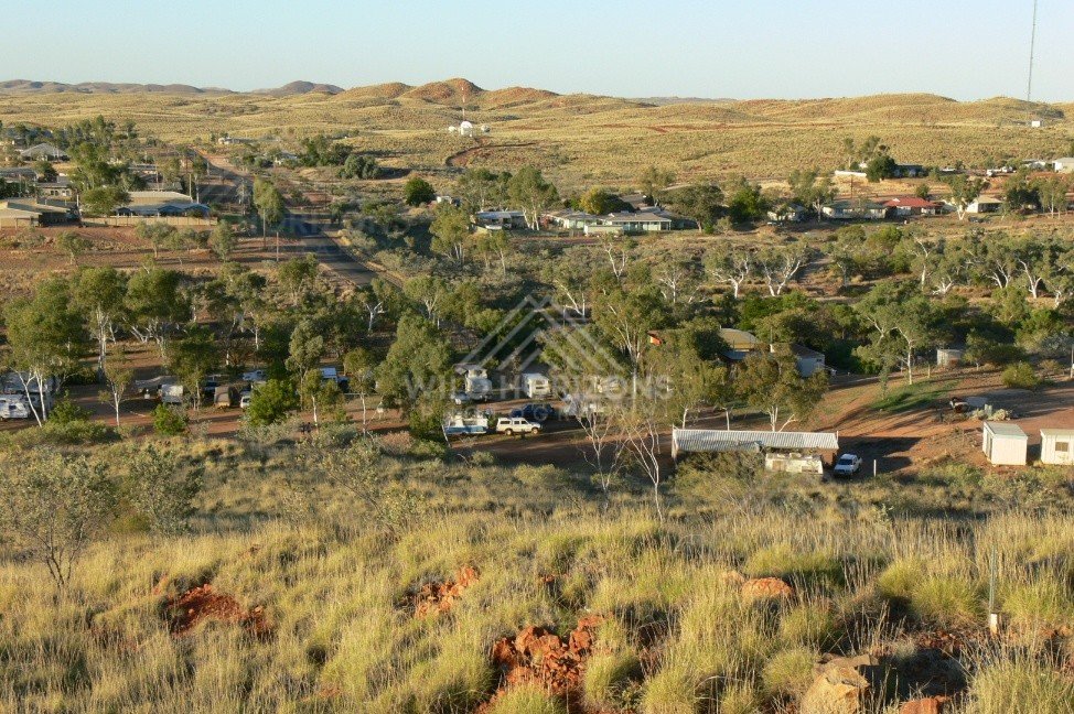 Outback township and caravan park among eucalypt trees with low ironstone hills beyond. Pilbara, Australia.