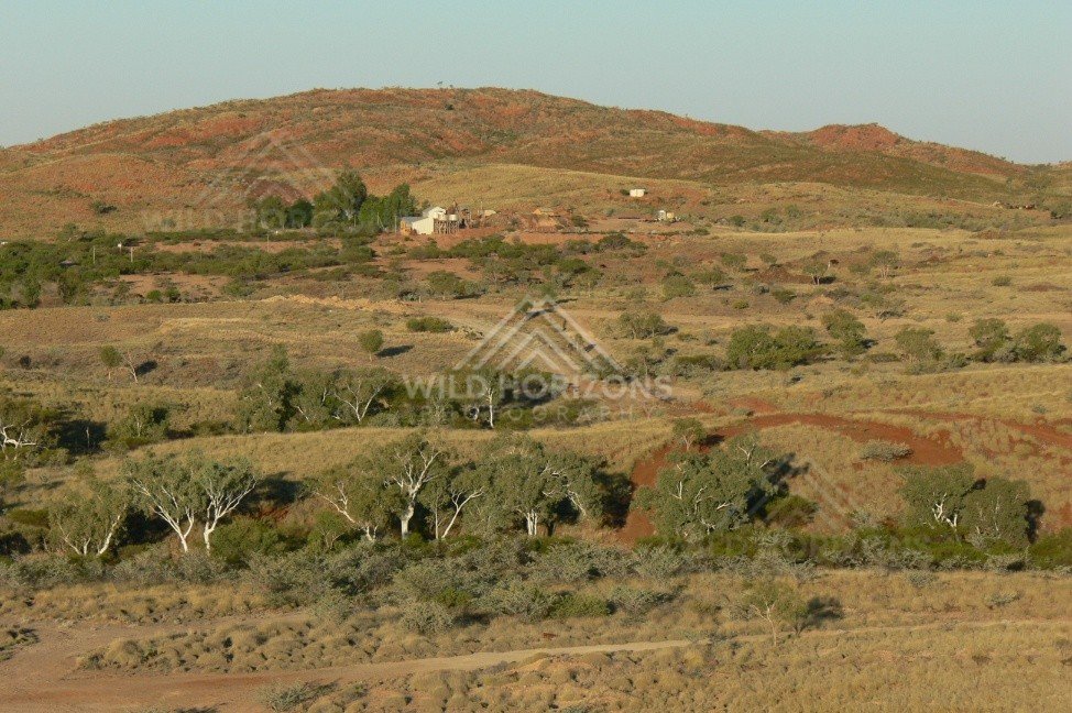 Isolated outback homestead set against red rocky hills and open grass plains. Pilbara, Australia.