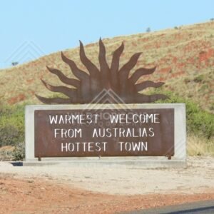 Roadside welcome sign with a steel sunburst reading “Warmest Welcome from Australia’s Hottest Town”. Marble Bar, Australia.