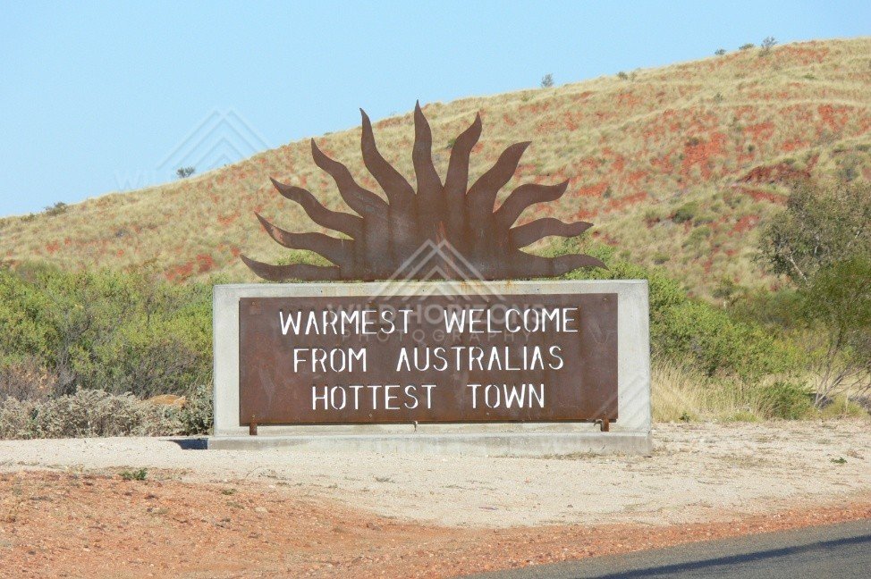 Roadside welcome sign with a steel sunburst reading “Warmest Welcome from Australia’s Hottest Town”. Marble Bar, Australia.