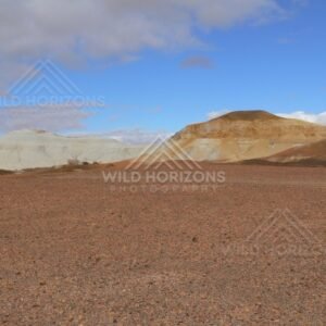 Broad desert vista toward sculpted Breakaways hills with blue sky clearing after cloud. Kanku-Breakaways Conservation Park/Coober Pedy, Australia.