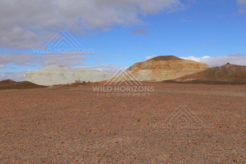 Broad desert vista toward sculpted Breakaways hills with blue sky clearing after cloud. Kanku-Breakaways Conservation Park/Coober Pedy, Australia.