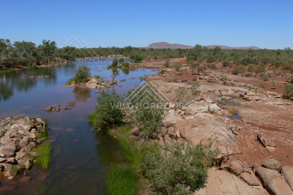 Outback river channel winding through red stony plains with scattered river gums. Central Australian interior, Australia.
