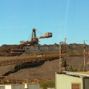 Iron-ore stacker and conveyor system beside dark stockpiles at a Pilbara mine site. Tom Price region, Australia.