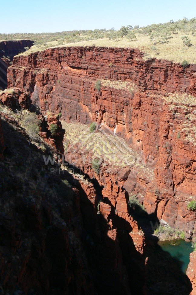 Sunlit ironstone escarpment above a Karijini gorge pool. Pilbara, Australia.