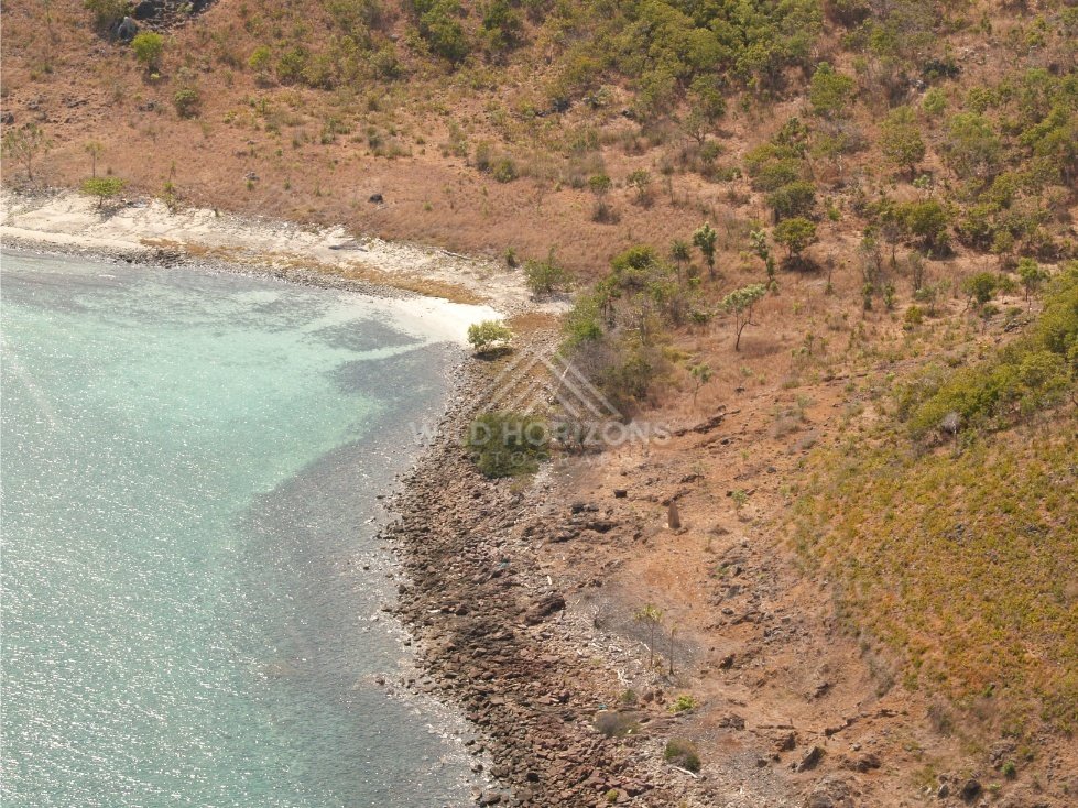 Curved pale beach and rocky shoreline seen from helicopter. Torres Strait, Queensland, Australia.