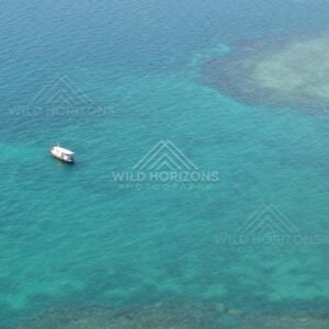 Small boat anchored over clear reef flats viewed from above. Torres Strait, Queensland, Australia.