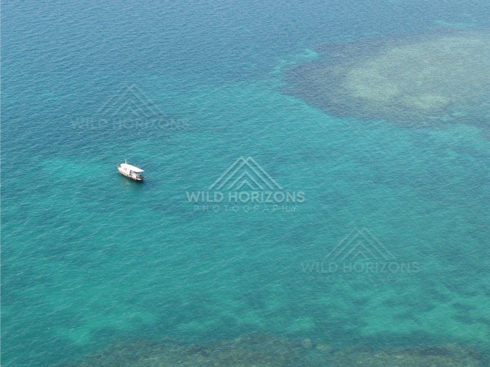 Small boat anchored over clear reef flats viewed from above. Torres Strait, Queensland, Australia.