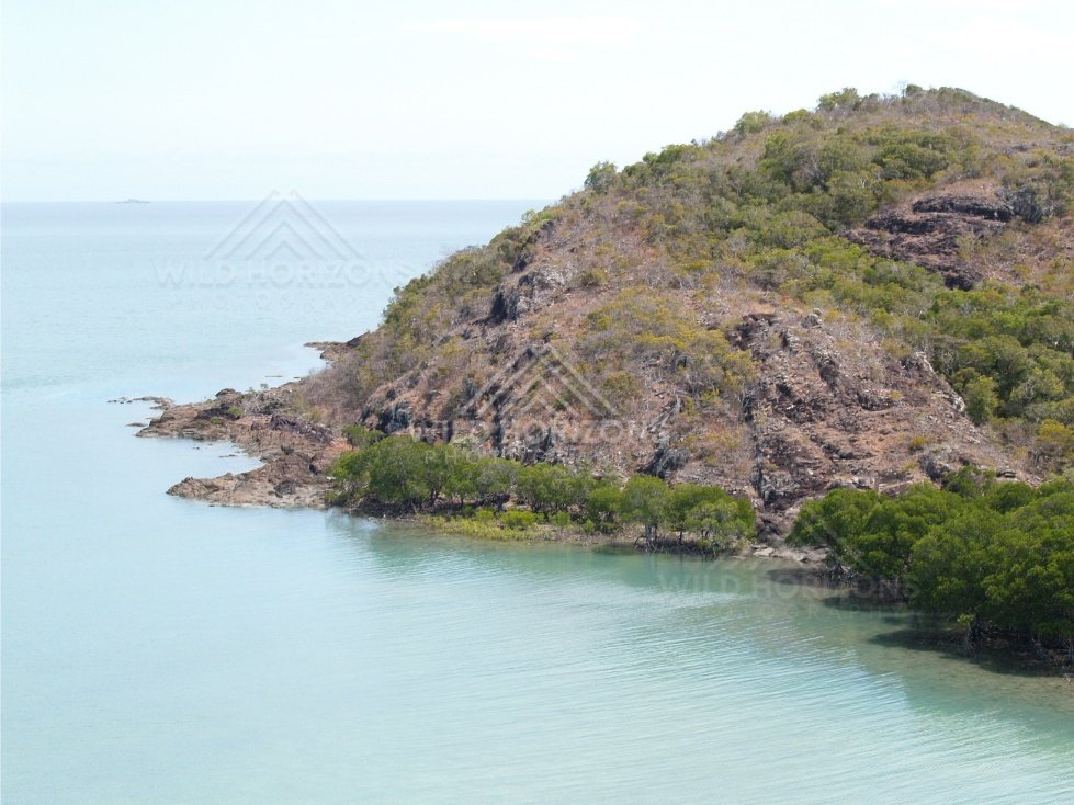 Rocky island headland rising from blue sea. Cape York, Queensland, Australia.
