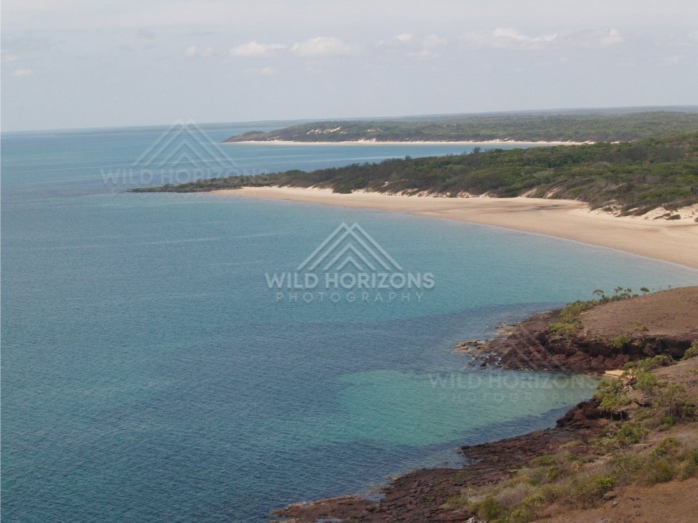 Wide bay with pale beach and forested dunes. Narau Beach, Queensland, Australia.