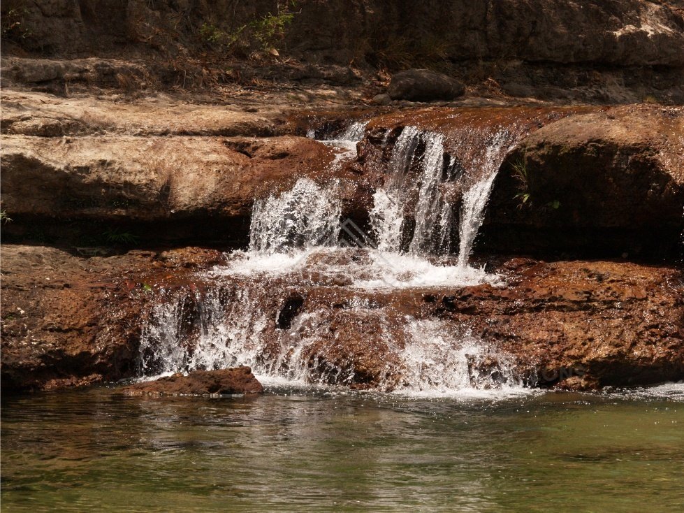 Multi-tiered waterfall across layered red rock. Fruitbat Falls, Queensland, Australia.