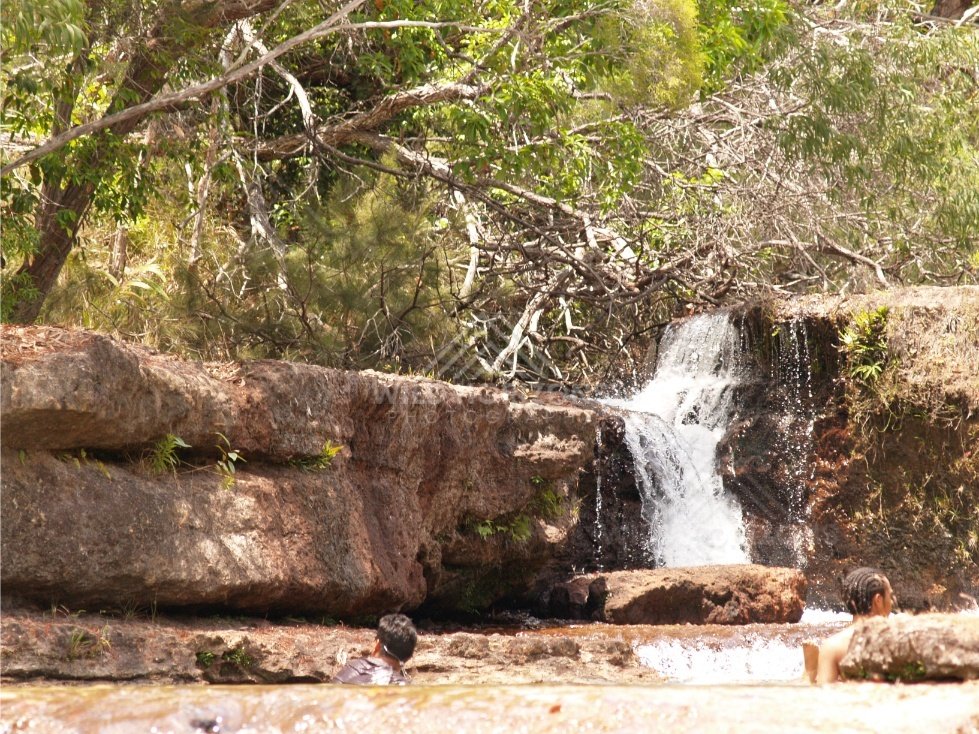 Small falls beside sandstone wall with people at pool edge. Fruitbat Falls, Queensland, Australia.