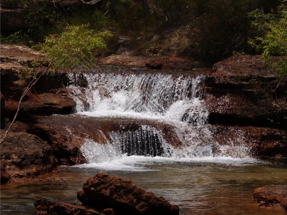 Broad step waterfall dropping into shaded pool. Fruitbat Falls, Queensland, Australia.