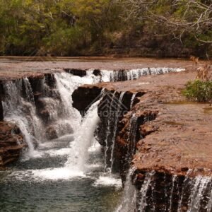 Ledge waterfall with textured red rock walls. Fruitbat Falls, Queensland, Australia.