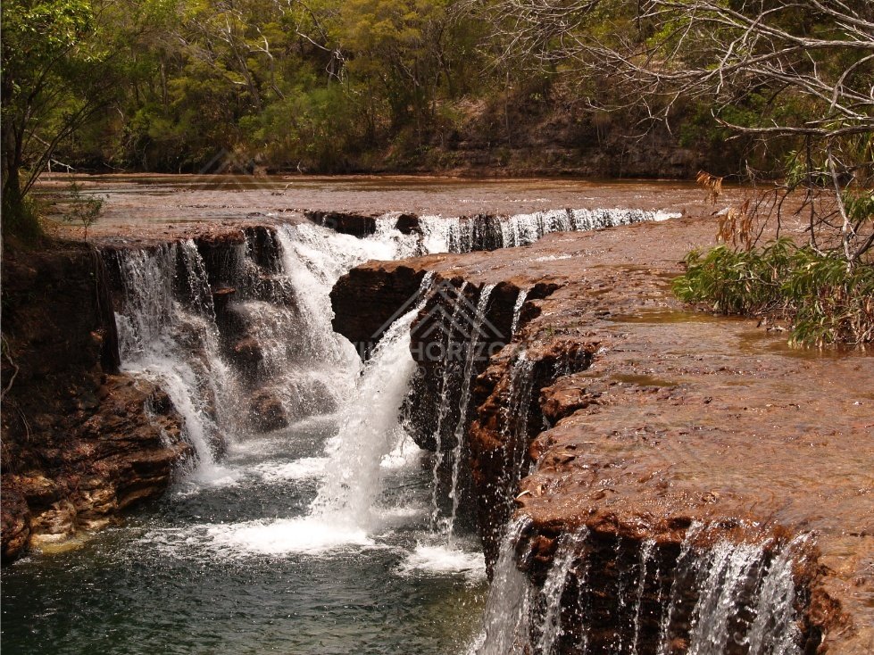 Ledge waterfall with textured red rock walls. Fruitbat Falls, Queensland, Australia.