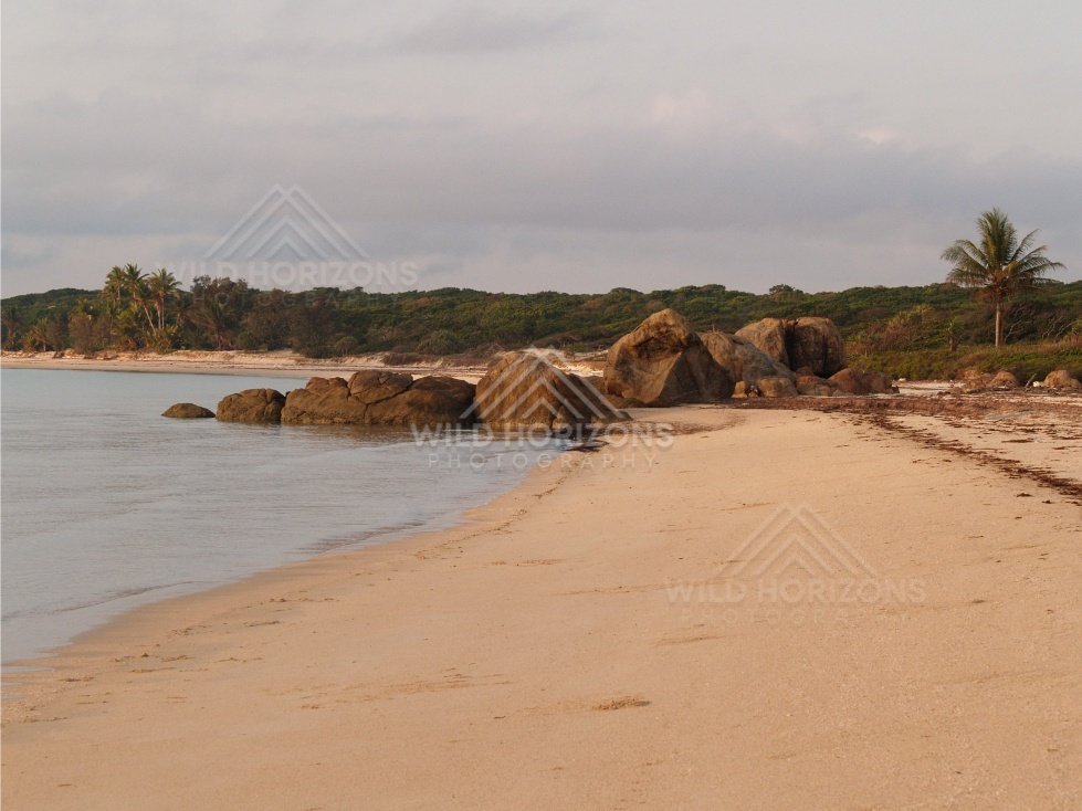 Sandy shoreline with rounded granite boulders and gentle surf. Portland Roads, Australia.