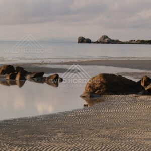 Reflections on shallow water with rocks and rippled sand at low tide. Portland Roads, Australia.