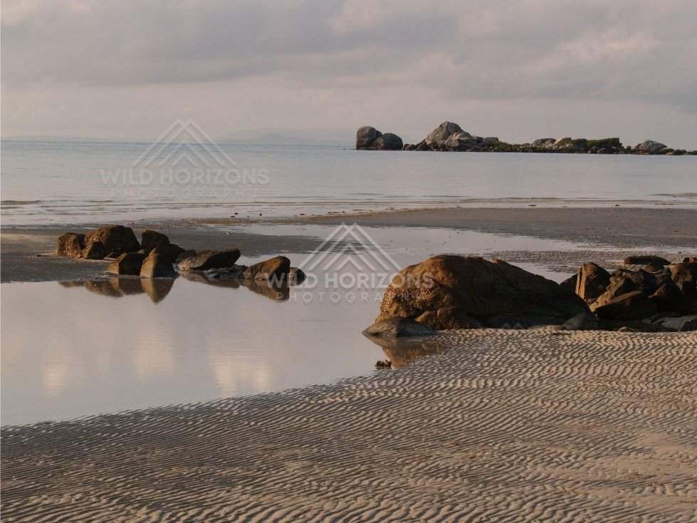 Reflections on shallow water with rocks and rippled sand at low tide. Portland Roads, Australia.