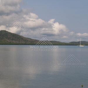 Calm bay with a distant sailboat beneath towering clouds. Portland Roads, Australia.