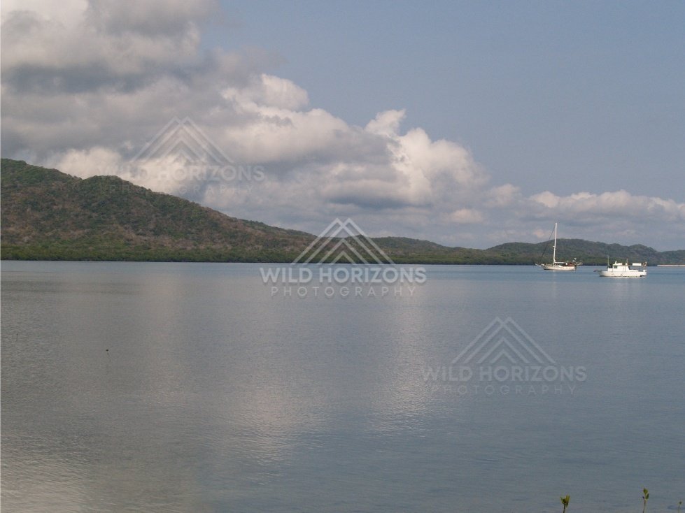 Calm bay with a distant sailboat beneath towering clouds. Portland Roads, Australia.