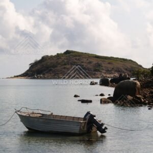 Small boat anchored in calm water near a rocky shoreline and headland. Portland Roads, Australia.