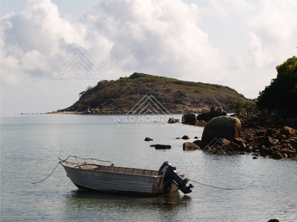 Small boat anchored in calm water near a rocky shoreline and headland. Portland Roads, Australia.