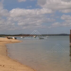 Curving shoreline with boats and weathered jetty pylons. Seisia, Queensland, Australia.