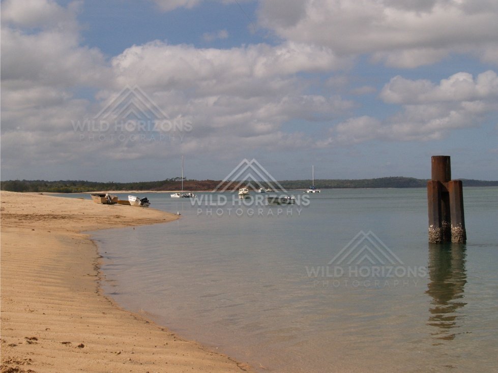 Curving shoreline with boats and weathered jetty pylons. Seisia, Queensland, Australia.