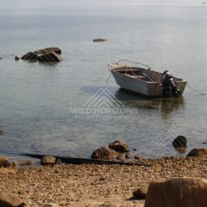 Beached dinghy beside scattered rocks on a quiet shoreline. Portland Roads, Australia.