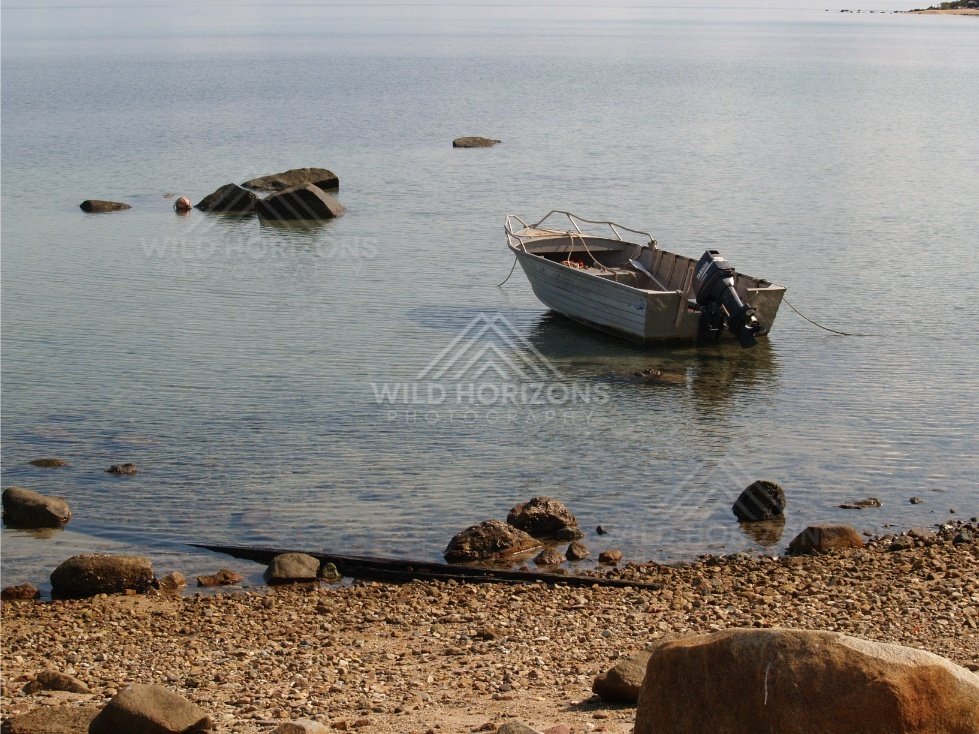 Beached dinghy beside scattered rocks on a quiet shoreline. Portland Roads, Australia.